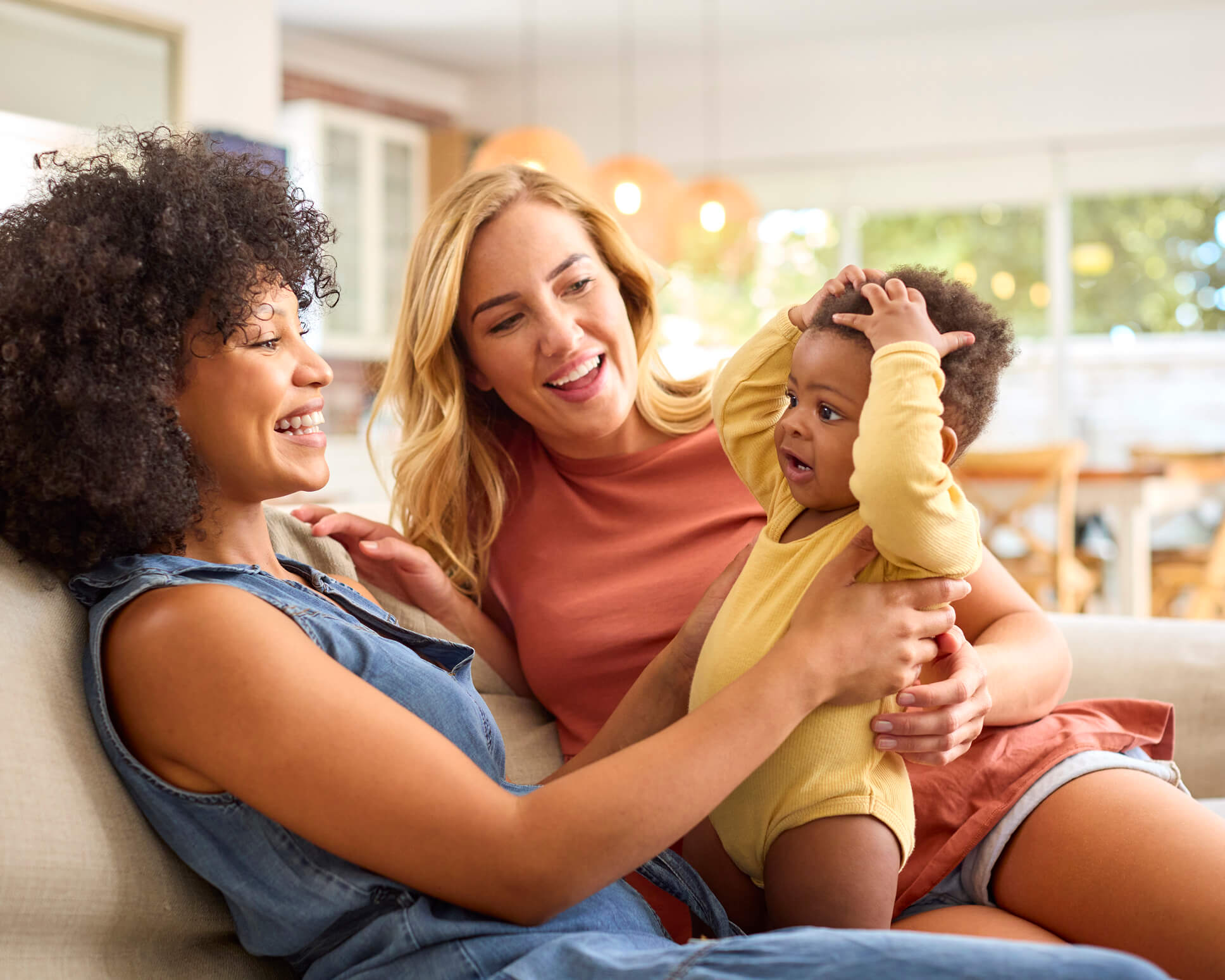 An LGBTQ+ couple smiles while holding their baby.