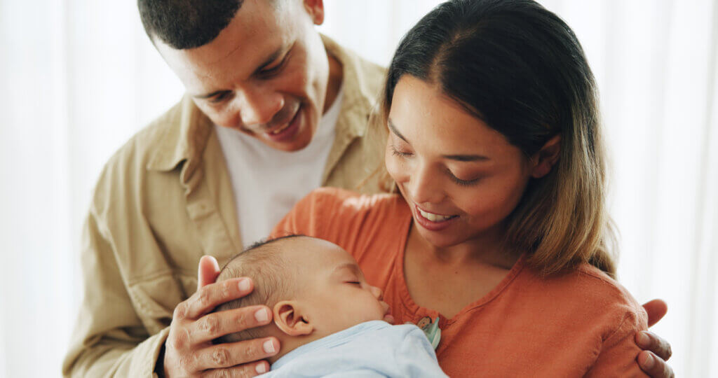 A man and a woman hold their baby and smile down lovingly.