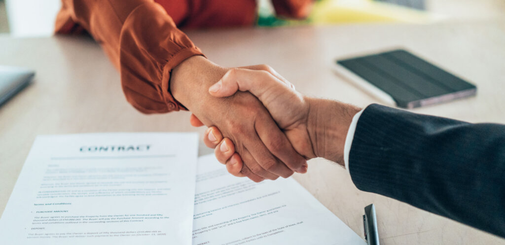 Two professionals shake hands over a signed contract.