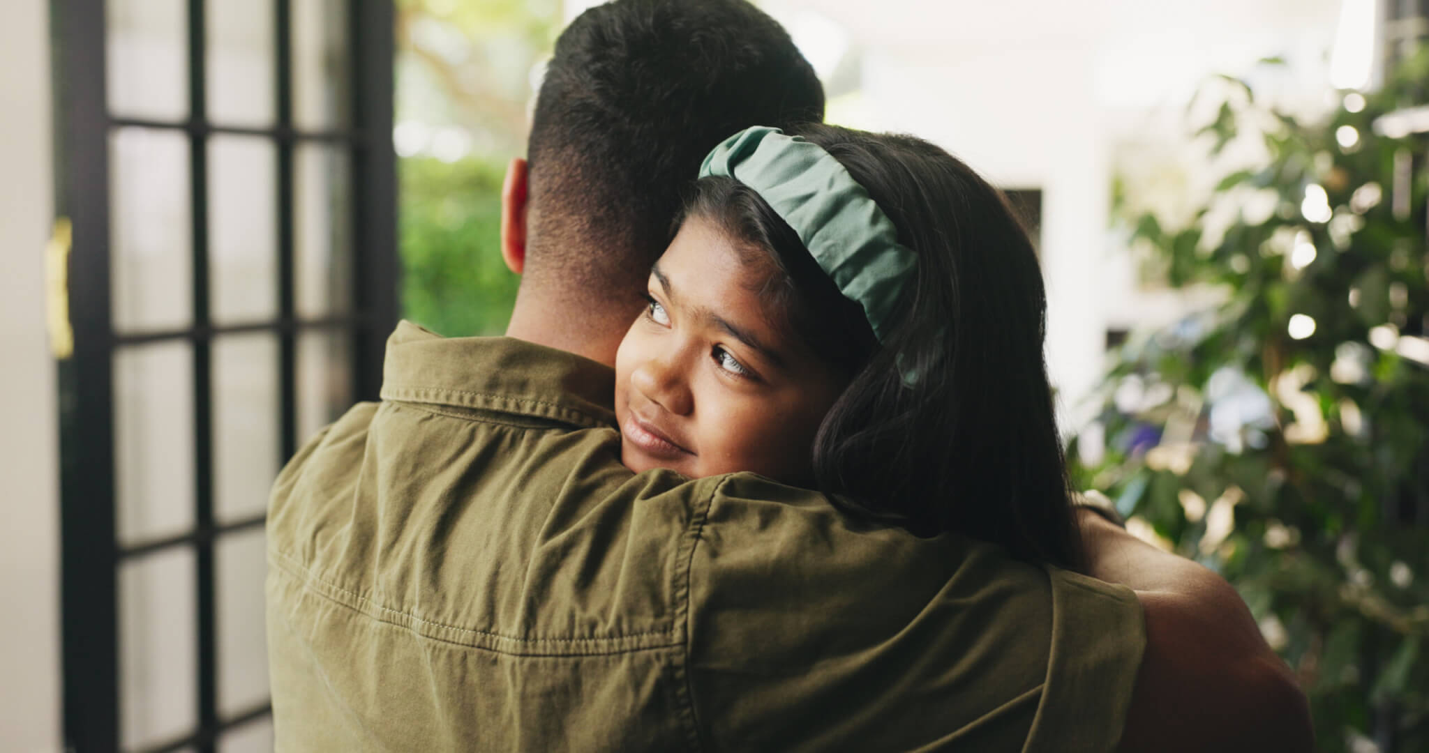An adult guardian hugs a young child in the doorway.