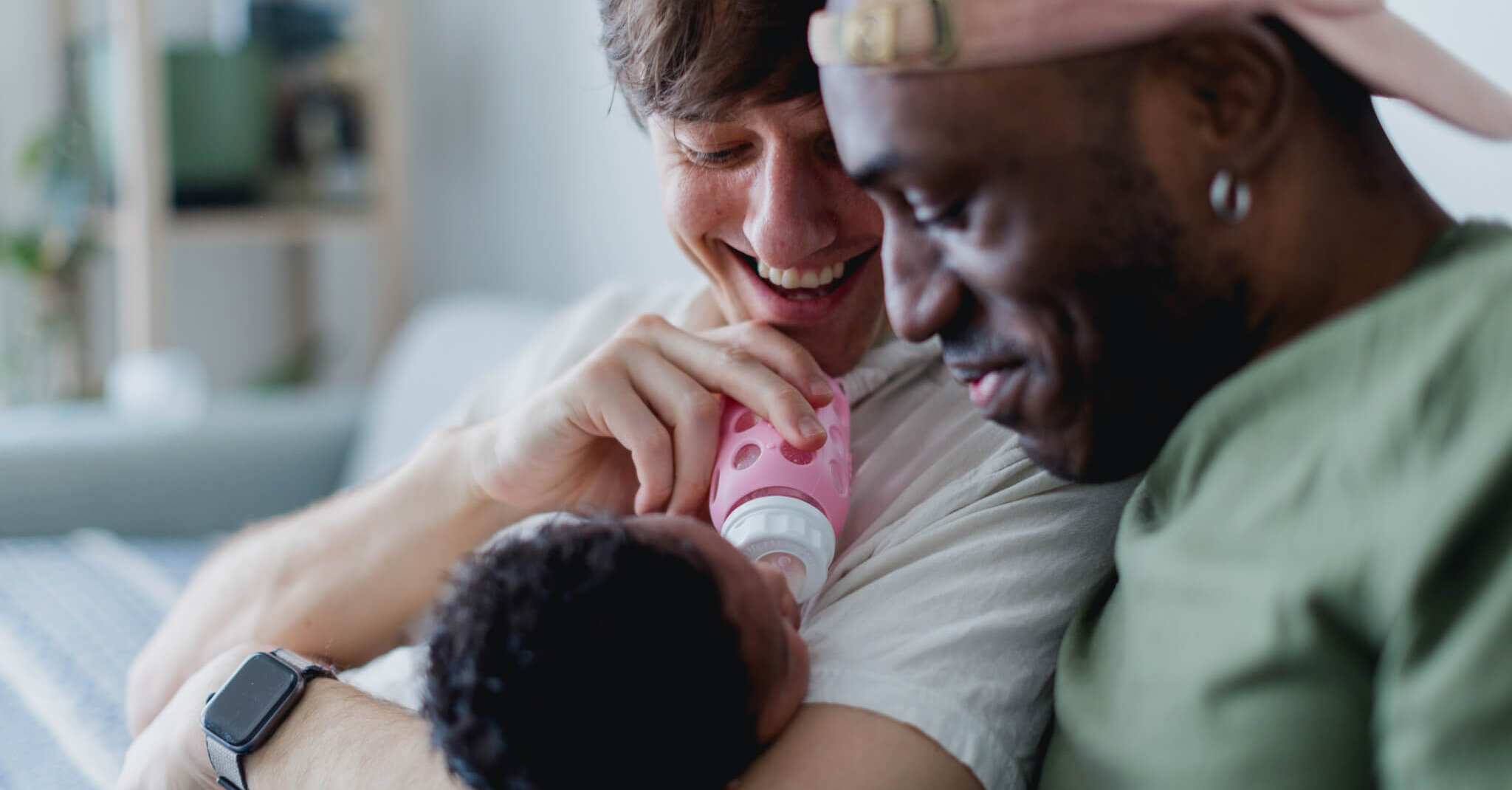 Two gay dads give their baby a bottle at home.