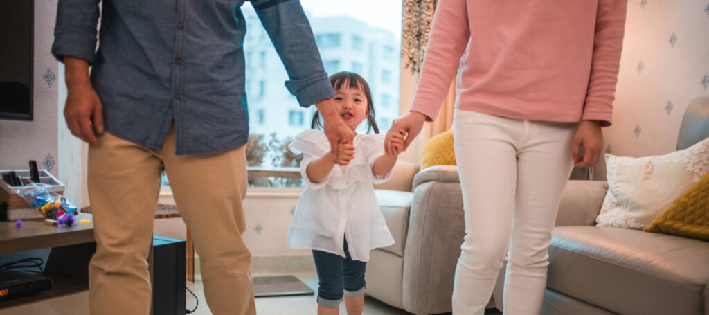 A young child holds both of her parents' hands.
